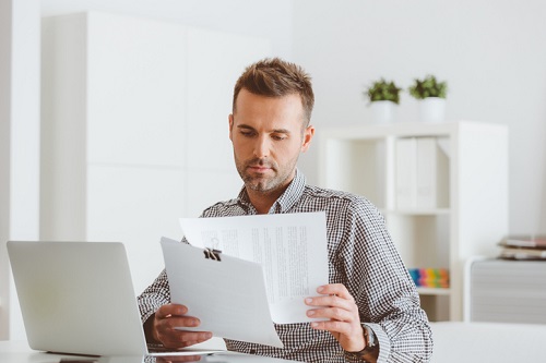 man sitting at computer looking at papers